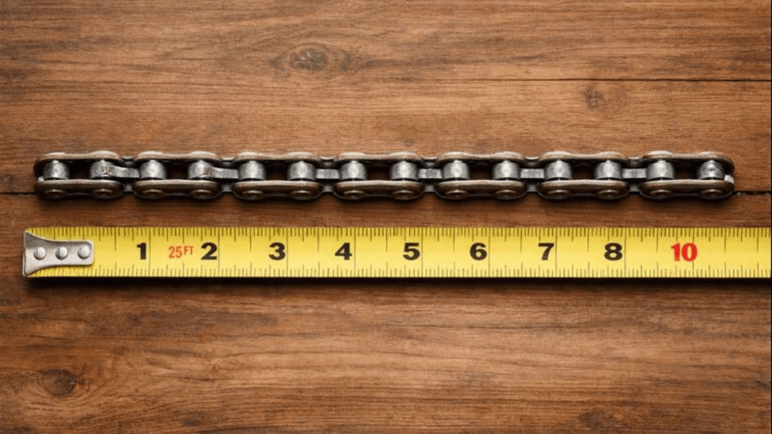 Close-up of a steel roller chain laid flat on a wooden surface with a measuring tape, showing how to measure chain size accurately.